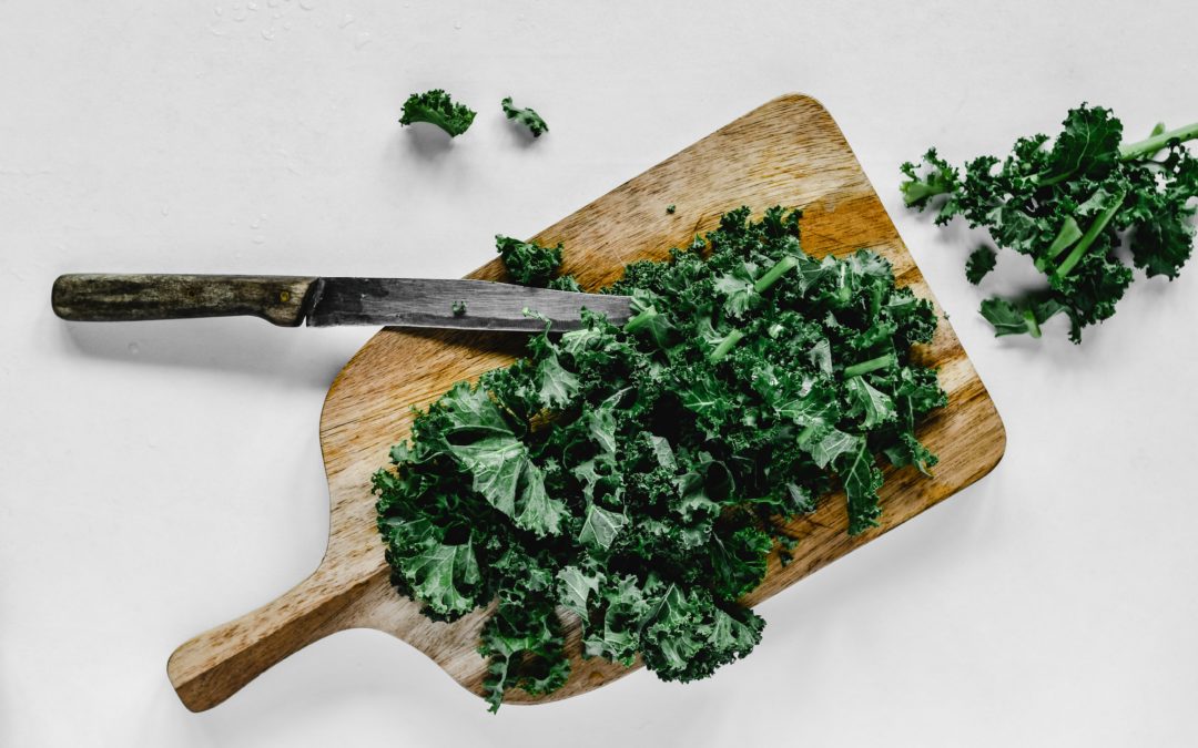 Knife chopping kale on a wooden cutting board